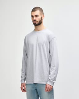 A long sleeve grey t-shirt displayed on a model wearing dark pants and white sneakers, featuring a logo.