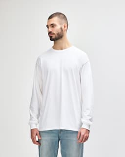 A white long sleeve T-shirt displayed on a model, featuring a round neckline and a logo on the sleeve.