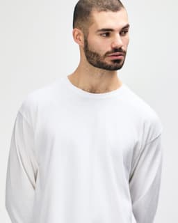 A white long sleeve t-shirt on a model, showcasing a classic fit and simple design. The shirt features a logo.