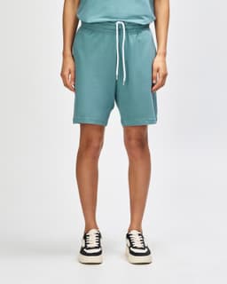 Unisex gym shorts in a soft teal colour, featuring an elastic waistband and pockets, paired with white sneakers.