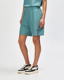 Unisex gym shorts in teal with pockets and a drawstring waistband, worn with white sneakers and socks.