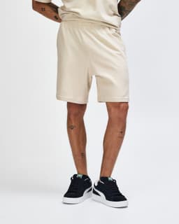 Beige unisex gym shorts with an elastic waistband and side pockets, worn with white sneakers and grey socks.