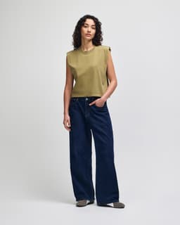 A woman is wearing an olive green muscle T-shirt paired with light blue baggy jeans. The outfit has a casual style.