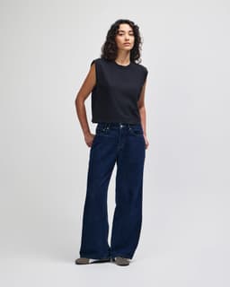 A grey women's muscle t-shirt paired with light blue baggy jeans and black and white sneakers.