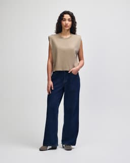A woman wearing an olive green muscle t-shirt paired with light blue cargo jeans. The shirt has a branding logo.