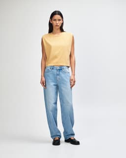 A mustard women's muscle T-shirt paired with light blue baggy jeans, featuring a logo.