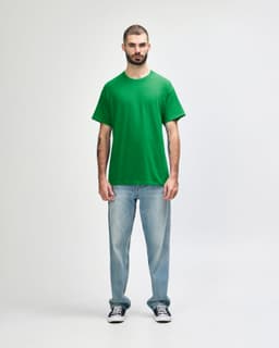 A green Gildan Heavy Cotton adult t-shirt displayed on a model wearing black jeans and sneakers, with a logo present.