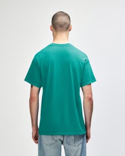 A man wearing a turquoise Gildan Heavy Cotton Adult T-Shirt, viewed from the back. The shirt has a logo.