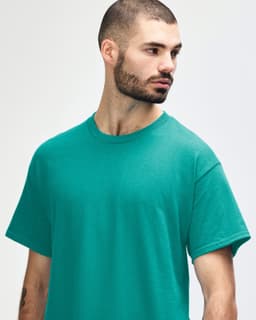 A turquoise Gildan Heavy Cotton Adult T-Shirt on a model, featuring a simple design and a logo.