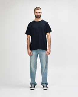 A black Gildan Heavy Cotton Adult T-Shirt worn by a model, paired with dark jeans and sneakers.
