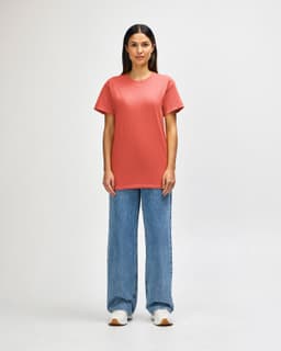 A model wearing a coral Gildan Heavy Cotton Adult T-Shirt paired with light blue jeans and white shoes.