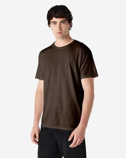 A man stands wearing a brown Gildan Heavy Cotton Adult T-Shirt. The shirt has a logo on it and a relaxed fit.