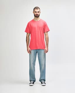 A coral Gildan Heavy Cotton Adult T-Shirt worn by a model, paired with black pants and casual sneakers.