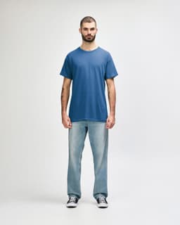 A man stands wearing a blue Gildan Heavy Cotton adult t-shirt and black jeans, with a logo on the shirt.
