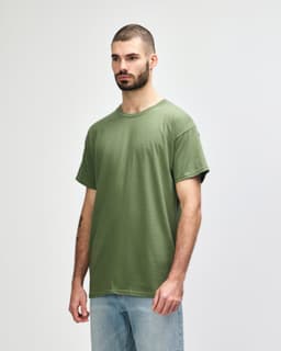 A man wearing a olive green Gildan Heavy Cotton Adult T-Shirt, standing against a neutral background.