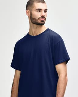 A navy Gildan Heavy Cotton adult T-shirt displayed on a model with short curly hair. The shirt has a simple design and branding.