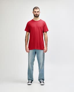 A red Gildan Heavy Cotton Adult T-Shirt worn by a model, paired with black jeans and sneakers. The shirt has a logo.