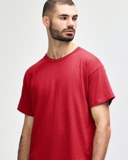 A plain red Gildan Heavy Cotton Adult T-Shirt displayed on a model, featuring a logo on the shirt.