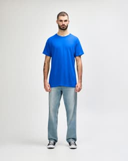 A man stands wearing a blue Gildan Heavy Cotton Adult T-Shirt paired with light blue jeans.