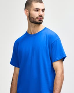 A man wearing a blue Gildan Heavy Cotton Adult T-Shirt. The shirt features a crew neckline and has a logo.