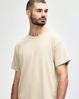 A beige Gildan Heavy Cotton Adult T-Shirt on a model, featuring a round neckline and a logo.