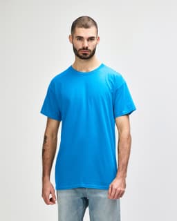 A man wears a turquoise Gildan Heavy Cotton Adult T-Shirt with short sleeves, standing against a plain background.