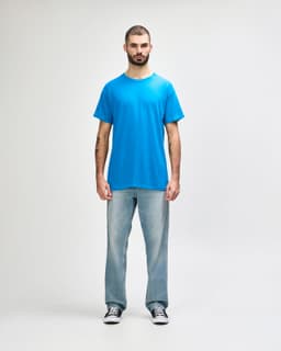 A blue Gildan Heavy Cotton adult t-shirt displayed on a model wearing black jeans and sneakers. The shirt has a logo.