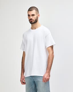 A white Gildan Heavy Cotton adult T-shirt displayed on a model with dark jeans. The shirt features a logo.