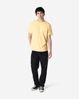 A man is wearing a yellow Gildan Heavy Cotton Adult T-Shirt paired with light blue jeans and white shoes.
