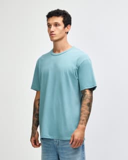 A unisex short sleeve T-shirt in a soft aqua blue colour, displayed on a model with tattoos. The shirt has a logo.