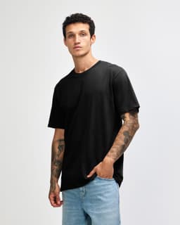 A black sueded unisex short sleeve T-shirt displayed on a model with tattoos, paired with light blue jeans.