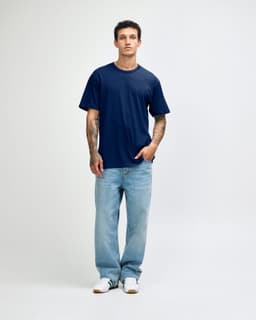 A navy blue unisex short sleeve T-shirt on a model, paired with light blue jeans. The shirt has a logo.