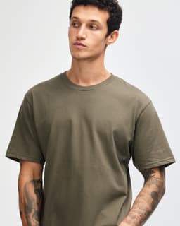 A model wearing an olive green unisex short sleeve t-shirt, featuring a logo on the shirt.