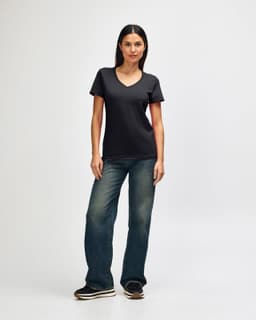 A model wearing a black Gildan Softstyle ladies' V-neck t-shirt paired with blue jeans and white shoes.