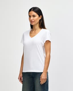 A white Gildan Softstyle ladies' V-neck T-shirt displayed on a model, paired with blue jeans. Features a logo.