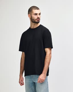 A black midweight t-shirt displayed on a model, featuring a simple design and a logo.