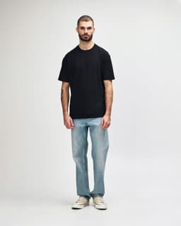 A black midweight t-shirt displayed on a model, paired with black jeans and sneakers. Features a logo.