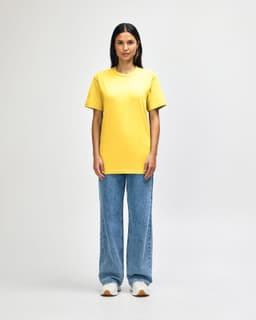 A midweight adult t-shirt in bright yellow, paired with black pants and black sneakers, featuring a logo.