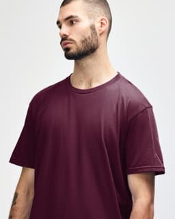 A man wearing a burgundy Gildan Softstyle adult midweight t-shirt, featuring a simple design and short sleeves.