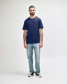 A man wearing a navy Gildan Softstyle adult midweight T-shirt and light blue jeans, standing against a plain background.