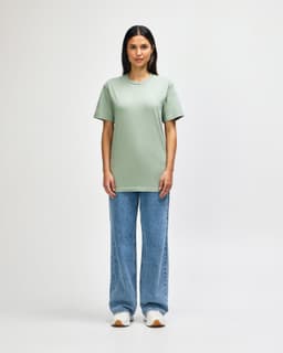 An olive green midweight t-shirt worn by a model, paired with black jeans and sneakers, featuring a logo.