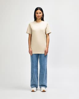 A light khaki midweight t-shirt is worn by a model paired with black pants and sneakers, also featuring a logo.