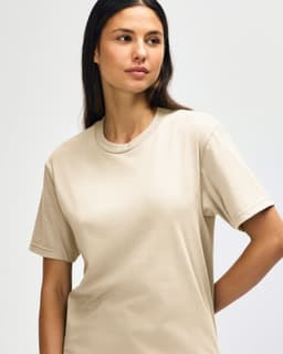 A midweight adult T-shirt in a neutral beige colour, displayed on a model with a casual pose. The shirt features a logo.