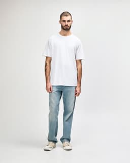A model wears a white midweight T-shirt paired with black jeans and sneakers, featuring a logo on the shirt.