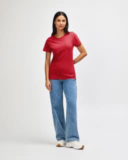 A red Gildan Softstyle ladies midweight T-shirt displayed on a model, paired with blue jeans and white shoes.