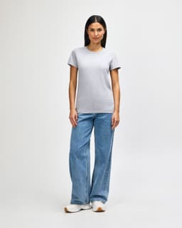 A grey midweight t-shirt on a model, paired with blue jeans and white shoes. The t-shirt has a logo.
