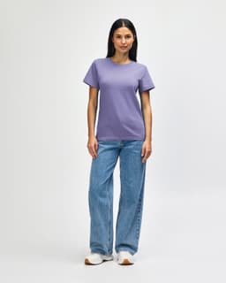 A purple midweight t-shirt is worn with blue jeans and white shoes, featuring a logo on the shirt.