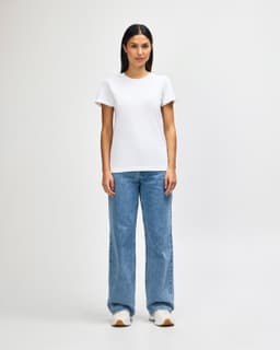 A model wearing a white ladies midweight T-shirt paired with blue jeans and white sneakers, standing in a neutral background.