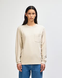 A lightweight, long-sleeve beige t-shirt featuring a pocket and a logo on the chest.