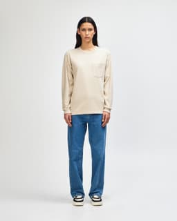 A model wearing a beige long-sleeve T-shirt with a pocket paired with olive green pants and casual sneakers.